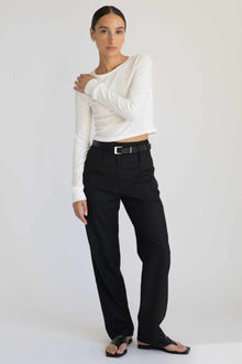 Woman wearing a white long-sleeve top and black pants against a white background