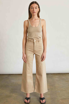 Woman wearing a beige tank top and wide-leg pants against a plain background