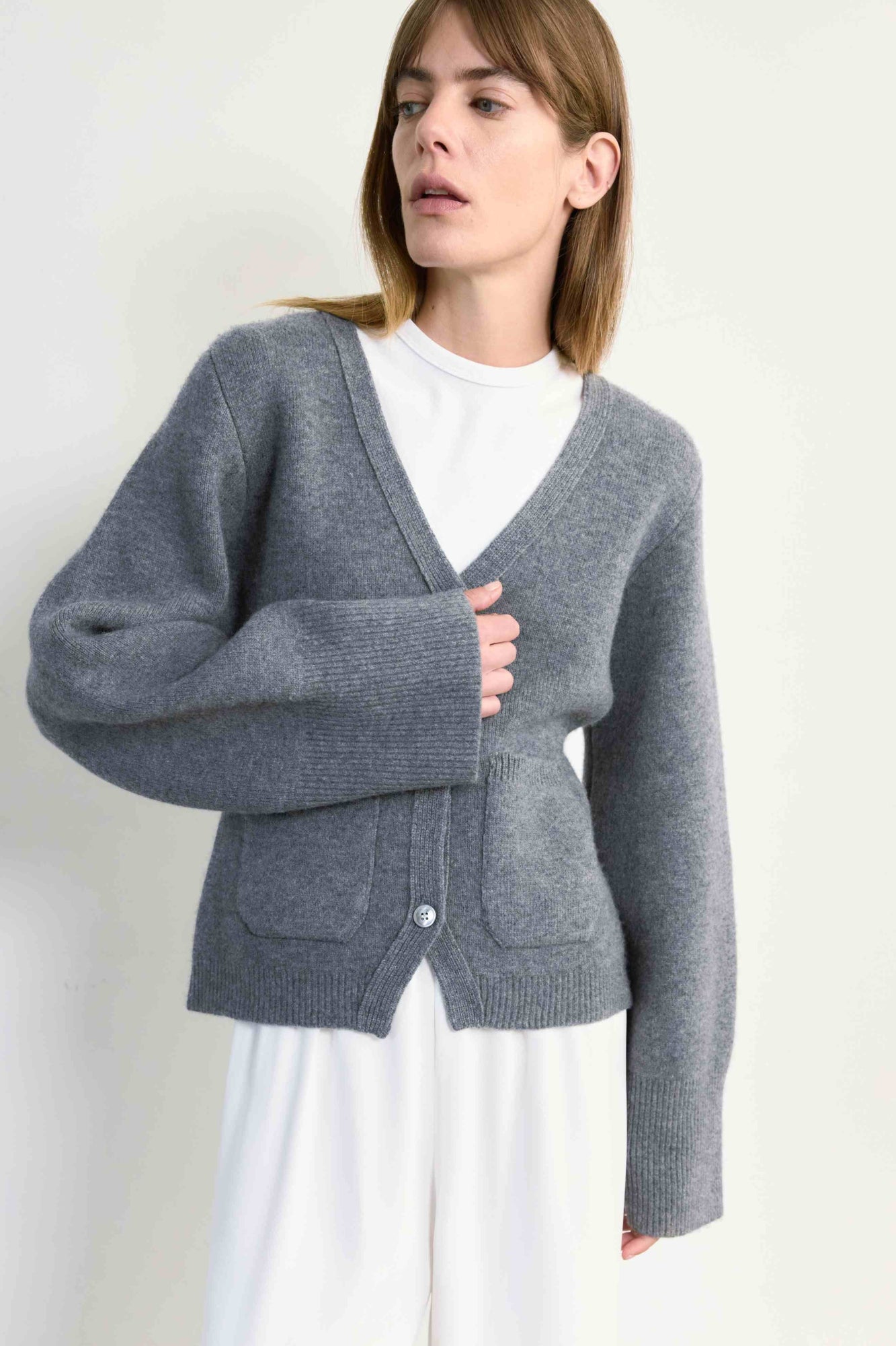 Woman wearing a gray cardigan over a white shirt on a plain background