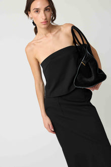 Woman wearing a black strapless top with a matching black skirt on a light grey background