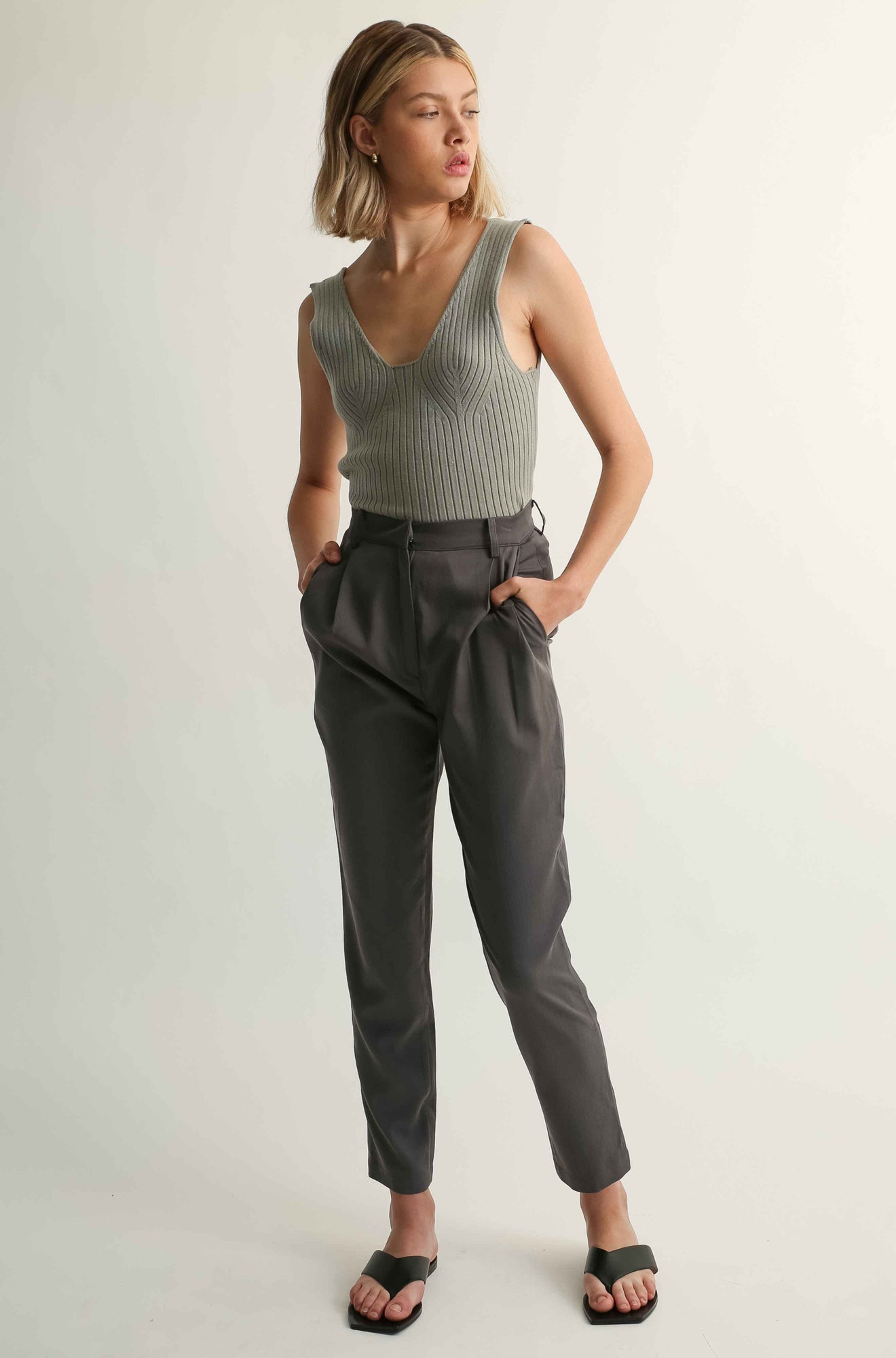 Woman wearing a sleeveless ribbed top and high-waisted pants on a light background