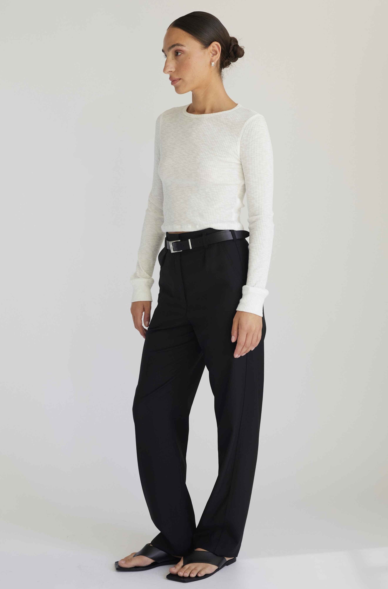 Woman wearing a white sweater and black pants on a plain background
