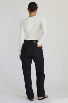 Person wearing a white long-sleeve shirt and black pants on a plain background