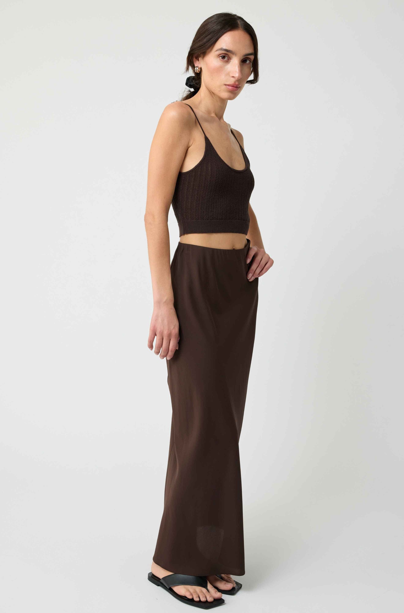 Woman wearing a brown sleeveless top and long skirt on a white background