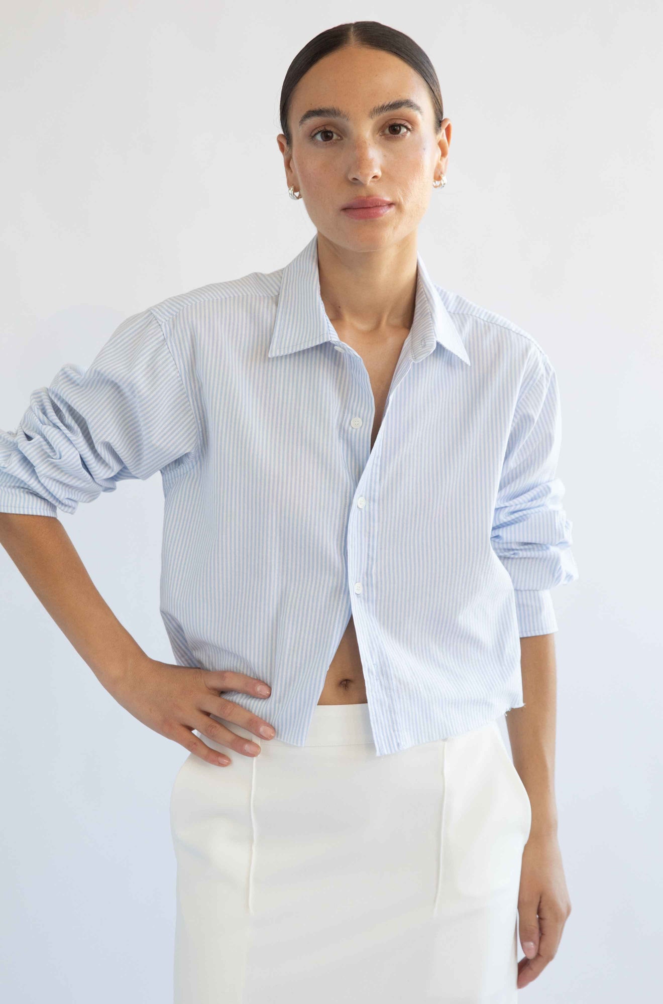 Woman wearing a light blue striped shirt and white pants against a plain background