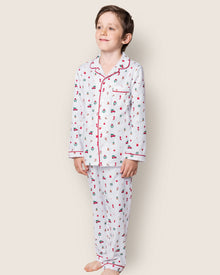 A young boy stands barefoot against a light background, wearing the Petite Plume Kids Twill Pajama Set in Winter Nostalgia, capturing the charm of Christmas bells.