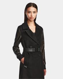 A woman with straight dark hair models the Rudsak MARYLIN - 8124520 Black women’s wool coat with leather sleeves, a wide collar, and a belted waist. She stands facing forward, her right hand in her pocket against a plain light background.