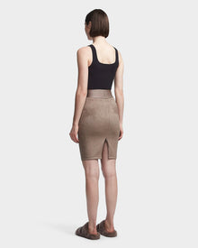 A person with short brown hair, in a black sleeveless top and the Rudsak CHEYNA - 8523514 Cement womens faux suede pencil skirt with a back slit, stands facing away against a plain light background, paired with brown slip-on shoes.