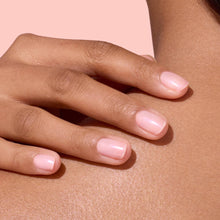 A close-up of a hand with neatly manicured nails painted light pink, gently resting on a persons shoulder against a soft pink background.
