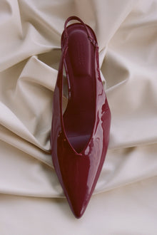Burgundy slingback kitten heel shoe with pointed toe, displayed from above on cream fabric.