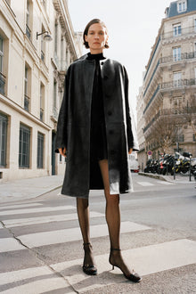 Black leather coat with button front and full-length silhouette worn over black turtleneck.