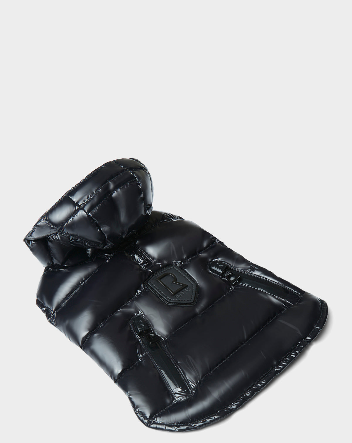 The Rudsak BUDDIE - 9122520 BLACK puffer, featuring a shiny black finish, high collar, and two zippered pockets, is displayed flat on a light gray background.
