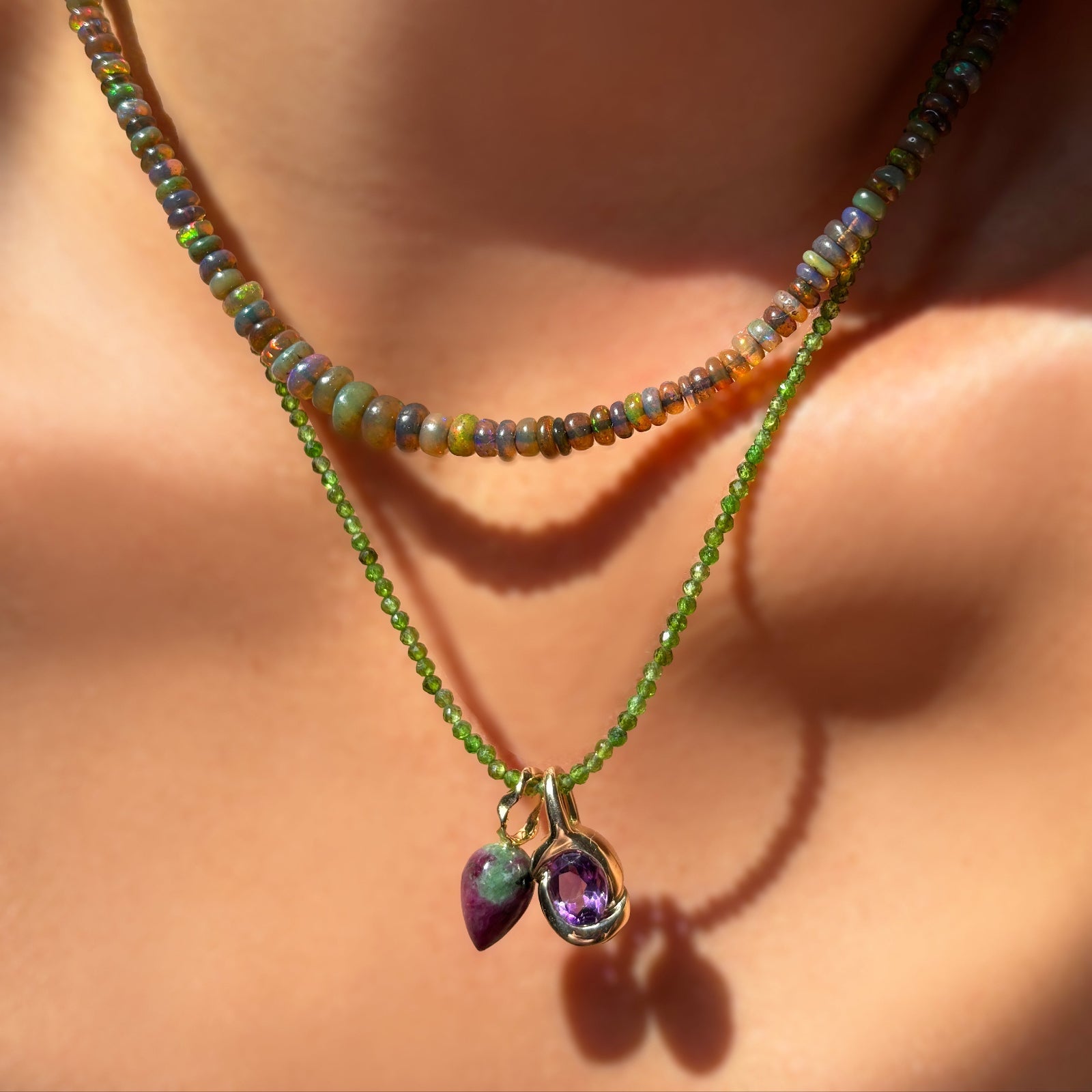 labradorite grey opal necklace styled with a slim gemstone necklace in green diopside with a ruby zoisite drop charm and knot charm with amethyst hanging on the neck.