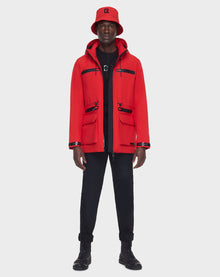 A person faces forward in the RUDSAK JACY - 6122000 POPPY RED mid-length raincoat and matching bucket hat, paired with black pants and boots, set against a plain light background.