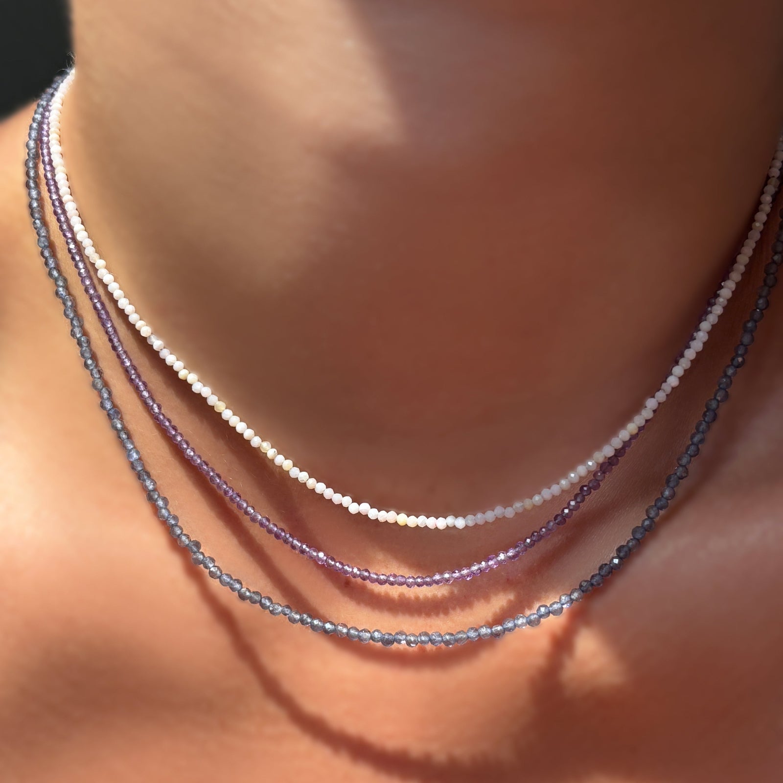 pink opal, amethyst, and iolite slim gemstone necklaces on the neck.