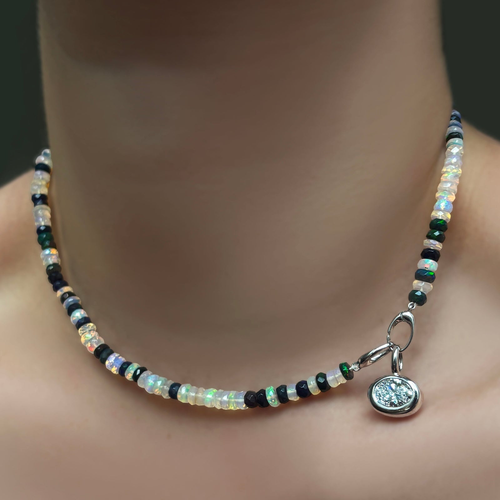 A small molten oval solitaire charm in the side turned clasp of a double shade welo opal necklace on a model's neck.