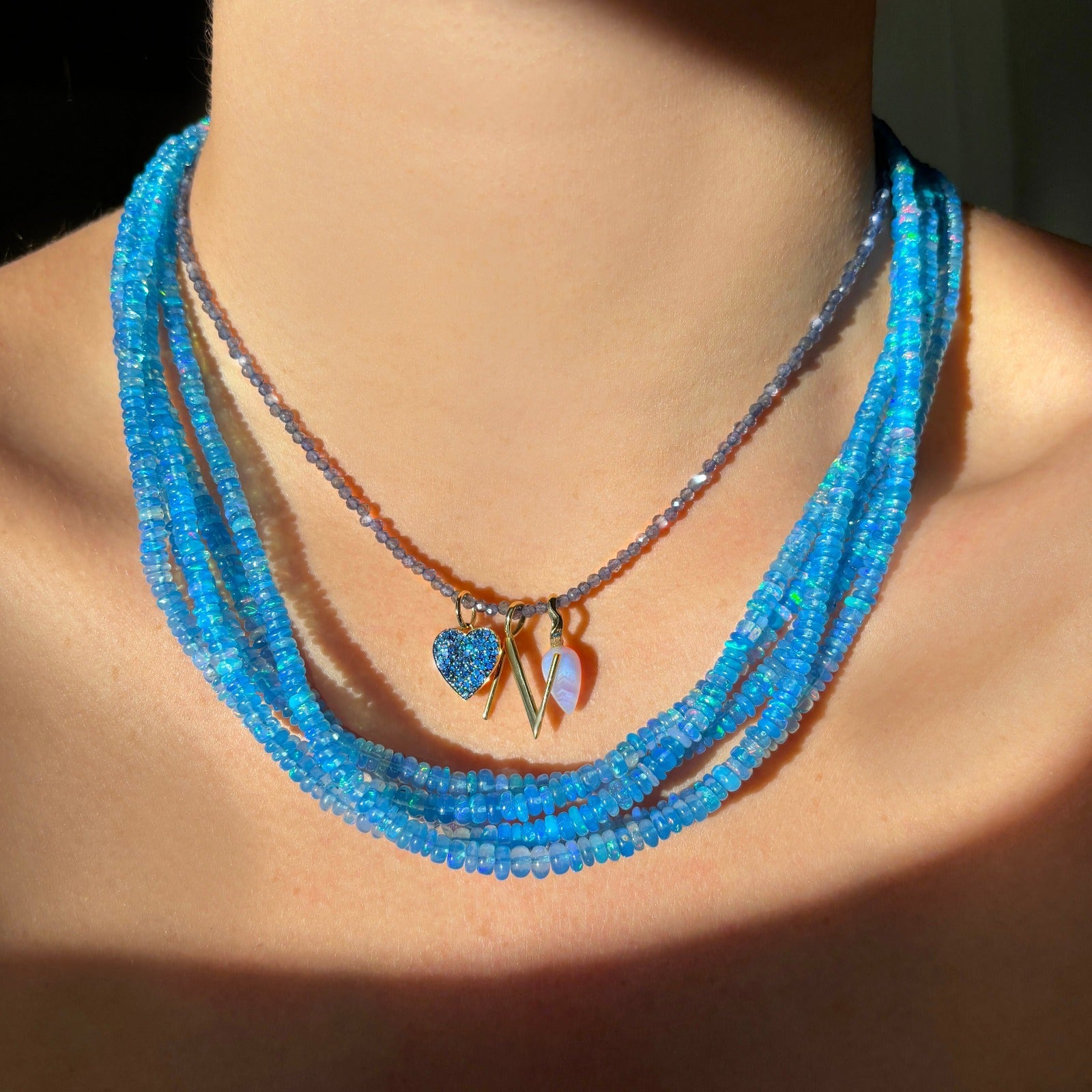 Shimmering beaded opal necklace made of smooth opals in shades of blue on a gold slim lobster clasp layered with a Iolite slim gemstone necklace with the blue lace agate acorn charm, Letter "N" Charm and Sapphire Pavé Heart Charm